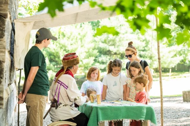 Children learning from a man dressed in period attire while a staffer and mom look on