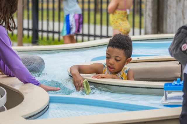 a child playing with a container in a river simulation at the splash pad